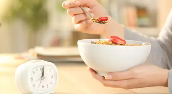 Une personne mange des céréales avec des fraises, une horloge à côté. Le jeûne intermittent avant après 1 mois, une nouvelle habitude alimentaire.