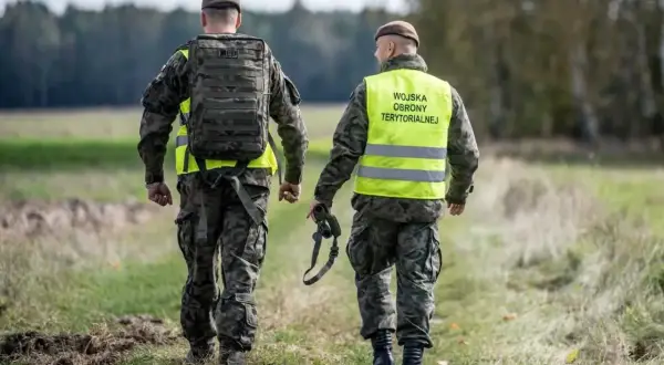 Dwóch żołnierzy Wojsk Obrony Terytorialnej w kamizelkach odblaskowych idzie przez pole. Rezygnacja z WOT może mieć poważne konsekwencje.