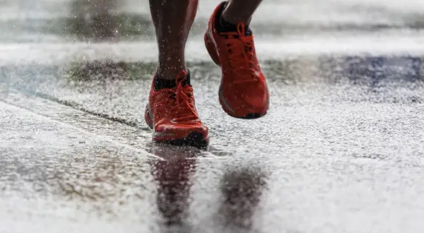 Scarpe da corsa arancioni che schizzano sull'asfalto bagnato, un'immagine di determinazione nel correre sotto la pioggia.