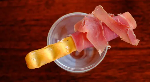 Ein knuspriger Grissini mit zartem Schinken, serviert in einem Glas.