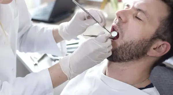 Dentysta bada zęby pacjenta. Rozważasz pokrycie recesji dziąsła NFZ? Wizyta u stomatologa to pierwszy krok.