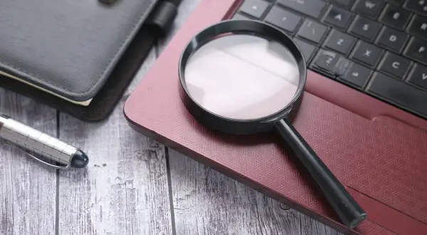 Lupa na laptopie, obok notatnika i długopisu. Szukam numeru seryjnego laptopa, by go zidentyfikować.