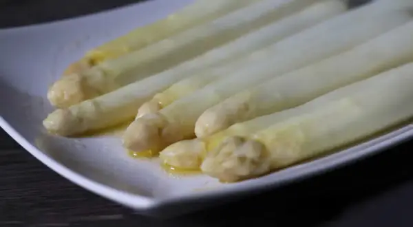 Zarte Spargelspitzen, perfekt gegart im Sous-Vide-Verfahren, liegen auf einer weißen Platte und glänzen in Butter.