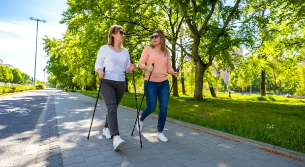 Deux femmes font de la marche nordique dans un parc ensoleillé, une activité idéale pour perdre du poids en marchant.