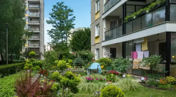 Zadbany ogródek we wspólnocie z kwitnącymi rabatami i zielenią, otoczony niskim ogrodzeniem.