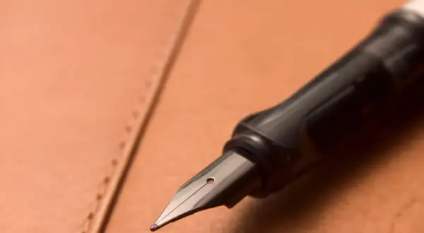 Plume d'un stylo plume noir sur un cuir brun. Une tache d'encre sur le cuir ? Apprenez comment enlever du stylo sur du cuir.