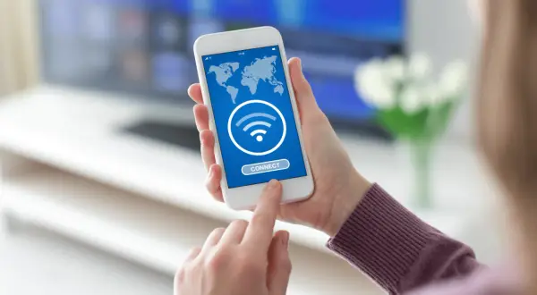 Dłoń trzyma smartfon z mapą świata i ikoną Wi-Fi. Dotyka przycisku "CONNECT", szukając darmowego hotspotu.