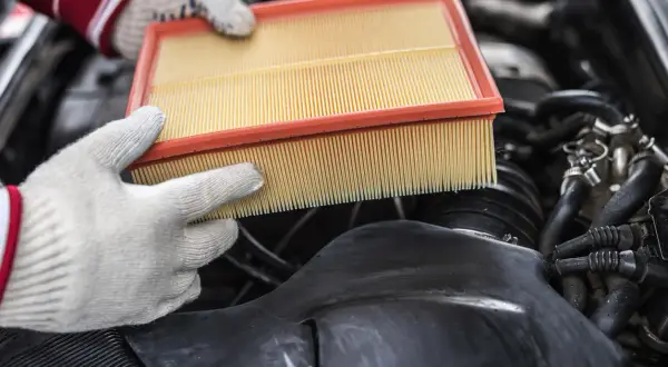 Mains gantées tenant un filtre à air propre, prêt à remplacer un filtre à air encrassé dans un moteur de voiture.
