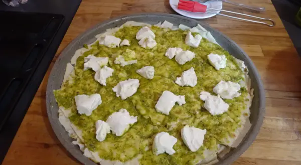 Une pizza à la pâte fine, recouverte de sauce verte et de morceaux de fromage blanc. Un délice inspiré du pain sarde.