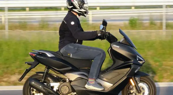 Osoba w kasku i kurtce jedzie na czarnym skuterze Keeway po drodze.