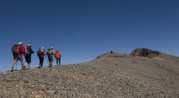 Randonneurs sur le flanc rocailleux du mont M'goun, sous un ciel bleu intense.