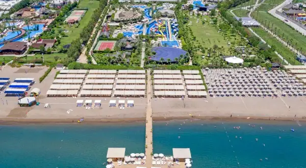 Widok z lotu ptaka na rozległy royal holiday palace z basenami, zjeżdżalniami, kortami tenisowymi i plażą z leżakami.