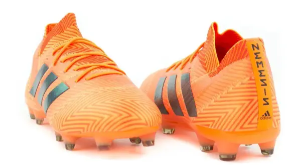 Pomarańczowe buty piłkarskie adidas Nemeziz 18.1 z czarnymi paskami i wzorem zygzak.