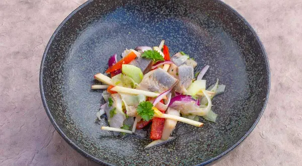 Heringssalat Hausfrauenart: ein deftiger Salat mit Hering, Apfel, Zwiebeln und Paprika in einer dunklen Schüssel.
