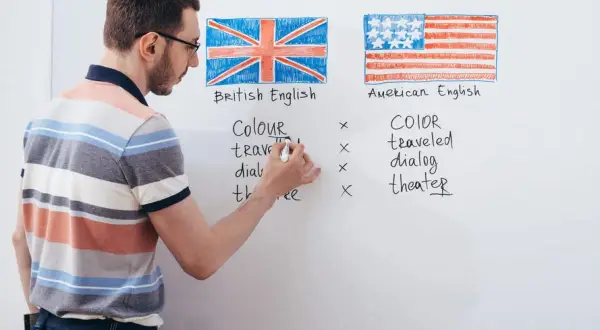 Profesor explica las diferencias de ortografía entre los tipos de inglés: británico y americano, con ejemplos escritos en la pizarra.