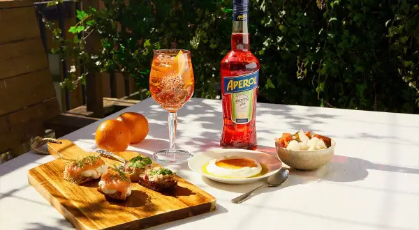 En Aperol Spritz med tilltugg till aperol spritz: laxsnittar, ost med honung och inlagda grönsaker.
