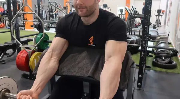 Mann trainiert Bizeps mit Langhantel im Fitnessstudio. Deutlich sichtbare Muskeln beim Bizeps dehnen.