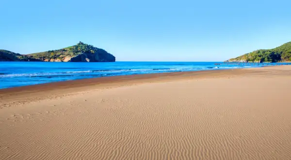 Piękna plaża w Sarigerme, z piaszczystym brzegiem i turkusowym morzem, w tle skaliste wzgórza.