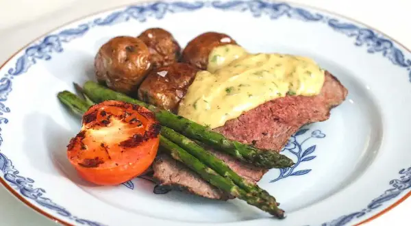 En tallrik med ryggbiff, potatis, sparris och tomat. En krämig sås toppar köttet. Ett perfekt ryggbiff recept!