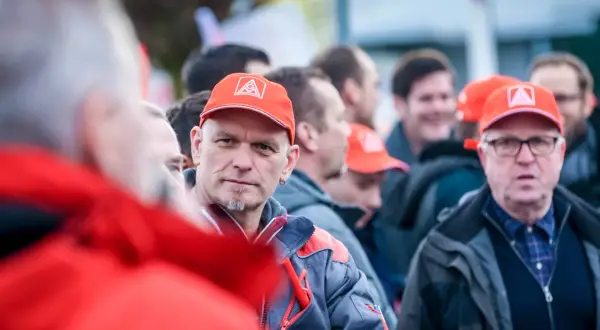 Männer in roten Kappen mit IG Metall Logo, diskutieren über die leistungszulage.