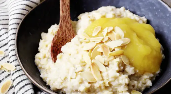 Reisflocken, cremig gekocht, mit Apfelmus und Mandelblättchen bestreut. Ein leckeres Frühstück, das zeigt, was Reisflocken sind.