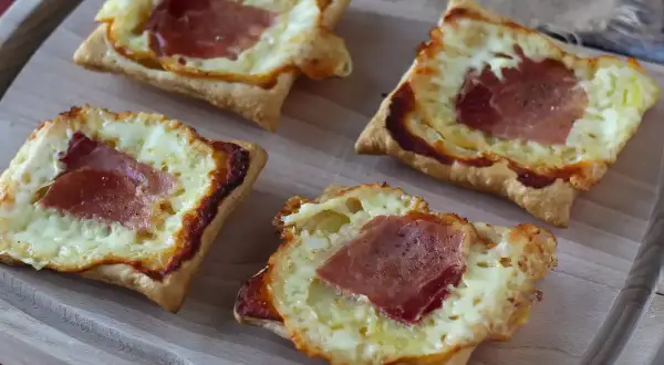 Cztery kwadratowe tartaletki z ciasta francuskiego, wypełnione roztopionym serem i plastrami szynki. Idealne na szybką przekąskę w stylu raclette.