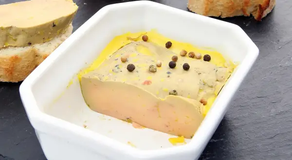 Un foie gras mi-cuit, à la texture parfaite, est servi dans un plat blanc, parsemé de grains de poivre. La température idéale pour savourer ce délice.