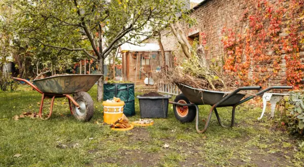 Gartenarbeit im Herbst: Schubkarren voller Laub und Äste warten darauf, kompost umsetzen zu helfen. Ein Eimer mit Küchenabfällen steht bereit.