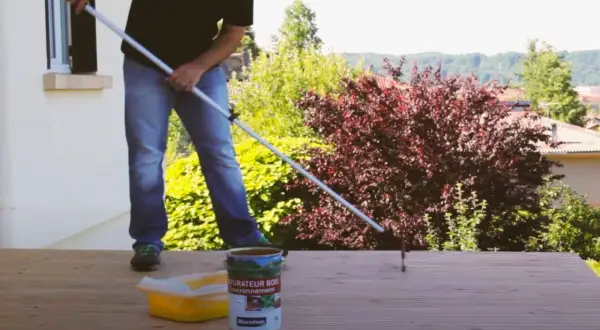 Application d'un saturateur sur une terrasse en bois. Le rouleau est en action pour un nettoyage et une protection parfaits.