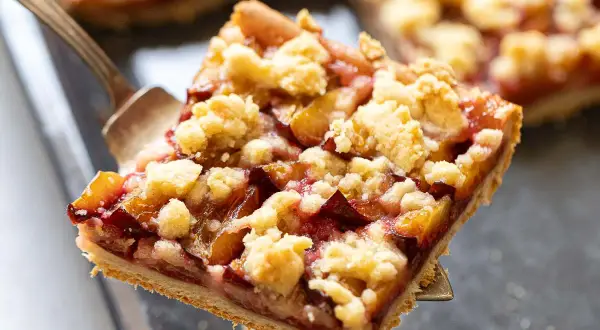Ein Stück Zwetschgendatschi mit Streuseln wird mit einer Tortengabel herausgehoben. Das Zwetschgendatschi Rezept ist einfach und lecker.