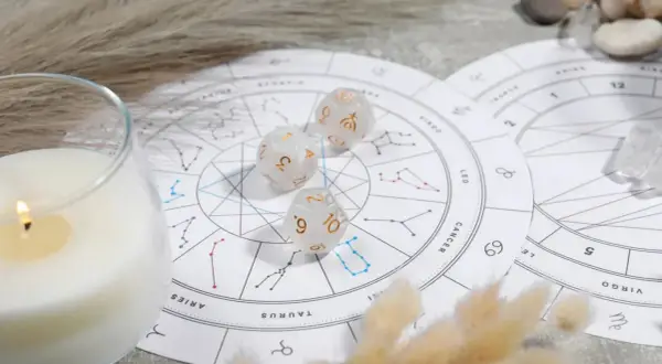Karty zodiaku, kostki z symbolami planet i płonąca świeca tworzą mistyczną atmosferę.