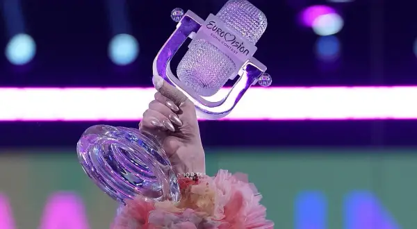 Ręka trzyma kryształowy mikrofon z logo Eurowizji, symbol zwycięstwa i historii konkursu.