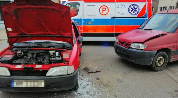 Wypadek po wymuszeniu pierwszeństwa. Dwa czerwone samochody po kolizji, obok karetka pogotowia.