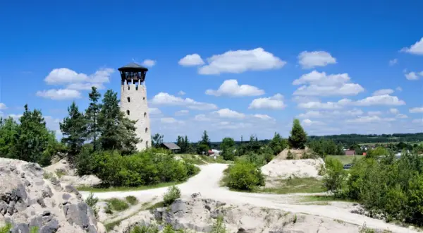 Kamienna wieża widokowa w Józefowie, otoczona zielenią i piaszczystymi wzniesieniami, zaprasza do podziwiania krajobrazu pod błękitnym, chmurowym niebem.
