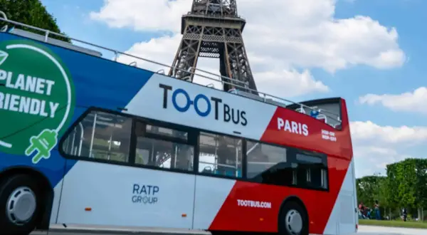 Ekologiczny autobus wycieczkowy Tootbus w Paryżu, z widoczną Wieżą Eiffla w tle. Idealny sposób na zwiedzanie Paryża samochodem.
