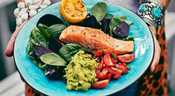 En matig sallad med lax, avokado, rödbetor, tomater och citron på en turkos tallrik.