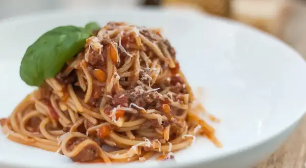 Pyszne spaghetti bolognese z parmezanem i listkiem bazylii na białym talerzu.
