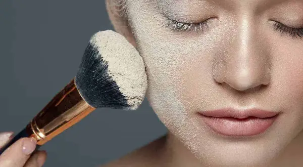 Un pennello applica cipria su un viso, mostrando la tecnica del "baking" per un trucco impeccabile.