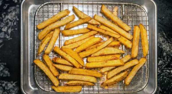 En hög med gyllene, krispiga pommes frites ligger på ett galler i en plåt. Perfekt för en snabb aptitretare.