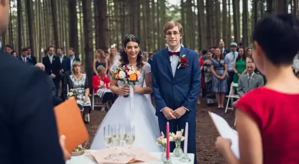 Para Młoda w lesie, goście czekają na ceremonię. Ile trwa ślub w kościele? To zależy, ale ta leśna przysięga jest wyjątkowa.