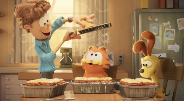 Jon reibt Käse für Lasagne, während Garfield und Odie gespannt zuschauen. Ein Festmahl für garfield – eine extra portion abenteuer!
