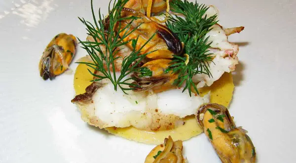 Délicieux plat de joue de lotte poêlée, garni de moules et d'aneth frais, servi sur un lit de purée.