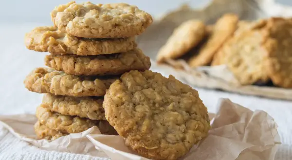 Ein Stapel goldbrauner Haferflocken-Bananen-Cookies auf einem weißen Tuch, daneben weitere Kekse.