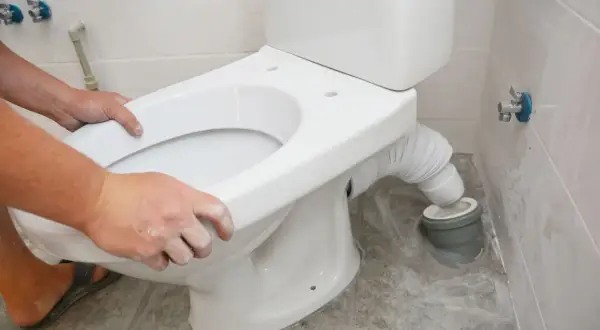 Montaż WC kompakt z odpływem pionowym: ręce przykładają deskę do sedesu, podłączając elastyczny wężyk do rury kanalizacyjnej.