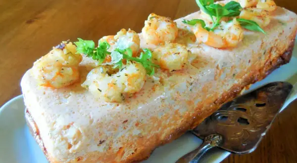 Un délicieux pain de poisson aux crevettes et herbes fraîches, prêt à être découpé avec une pelle à tarte ornée.