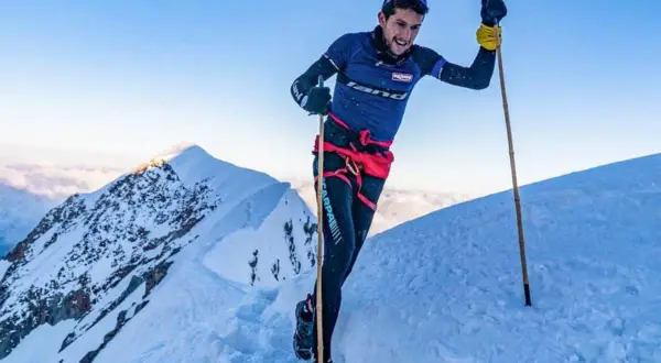 Manuel Merillas, le coureur de trail, franchit une crête enneigée, bâtons en main, sous un ciel bleu éclatant.