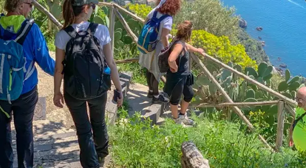 Gruppo di escursionisti sul sentiero degli dei ad Agerola, con vista sul mare blu e vegetazione mediterranea.