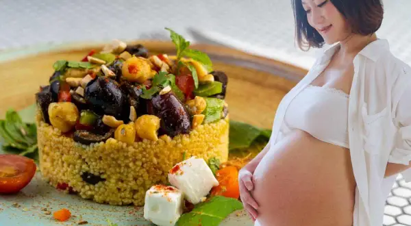 Piatto colorato di cous cous con verdure e formaggio, accanto a una donna incinta. Un pasto nutriente per la gravidanza.
