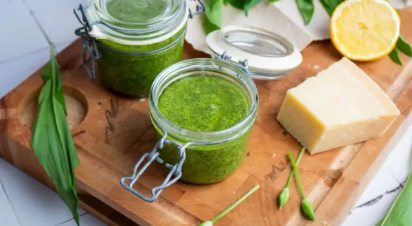 Frisches Bärlauchpesto in Gläsern, bereit für ein köstliches pesto rezept. Daneben ein Stück Parmesan, Zitrone und Bärlauch.