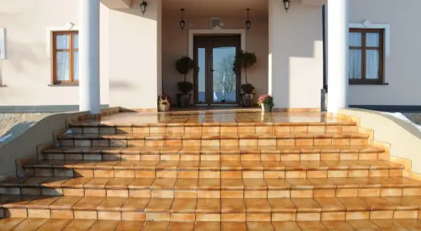 Amplias escaleras de entrada a un chalet, con escalones de baldosas naranjas que brillan bajo el sol.